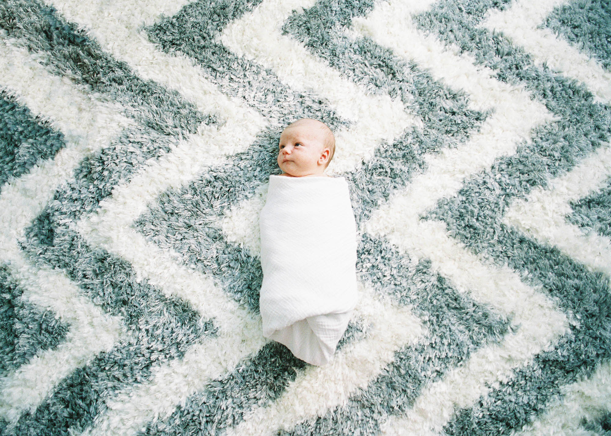 newborn baby boy lies down on a chevron rug