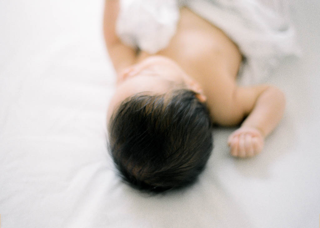 A newborn baby girl is asleep on a set of what sheets. This photo is focused not he top of the baby's head and shows off her full head of dark hair.