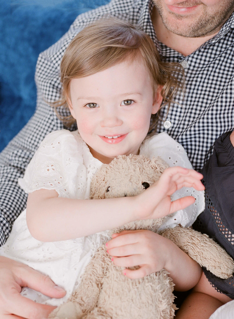 toddler cuddles her teddy bear and smiles at the camera